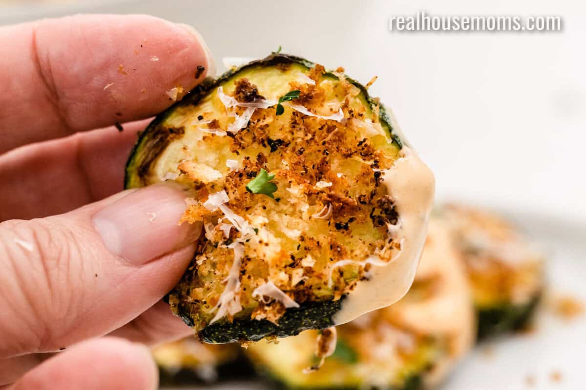 close up of a hand holding a slice of Air Fryer Parmesan Zucchini after dipping it in sauce