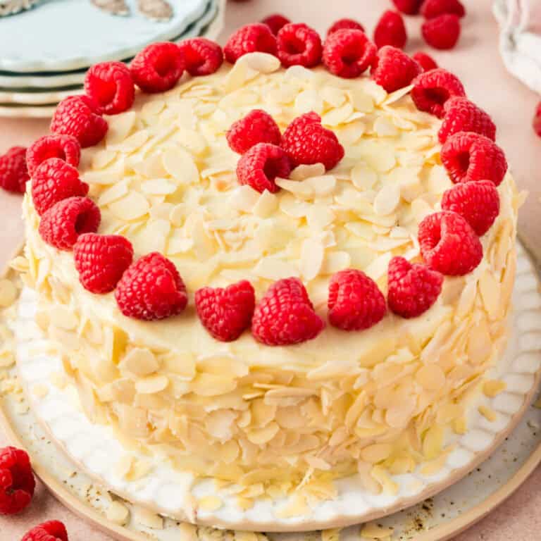 square image of a almond raspberry cake with sliced almonds and raspberries for garnish