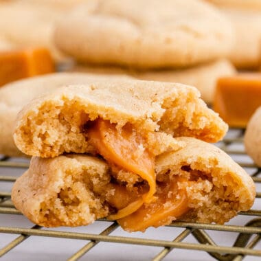 square image of a apple cider cookie with caramel filling broken in half to show to gooey caramel inside