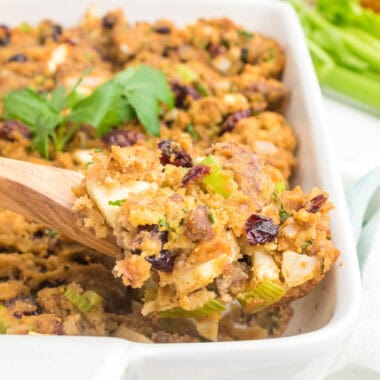 square image of a serving spoonful of apple & cranberry cornbread dressing over the baking dish