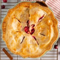 square image of apple cranberry pie in a pie plate with a pie serve starting to remove a slice