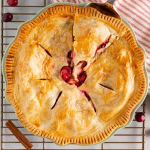 square image of apple cranberry pie in a pie plate with a pie serve starting to remove a slice
