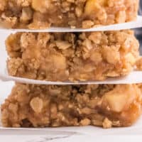 stack of three apple pie oatmeal bars with pachment paper between each bar with recipe name at the bottom