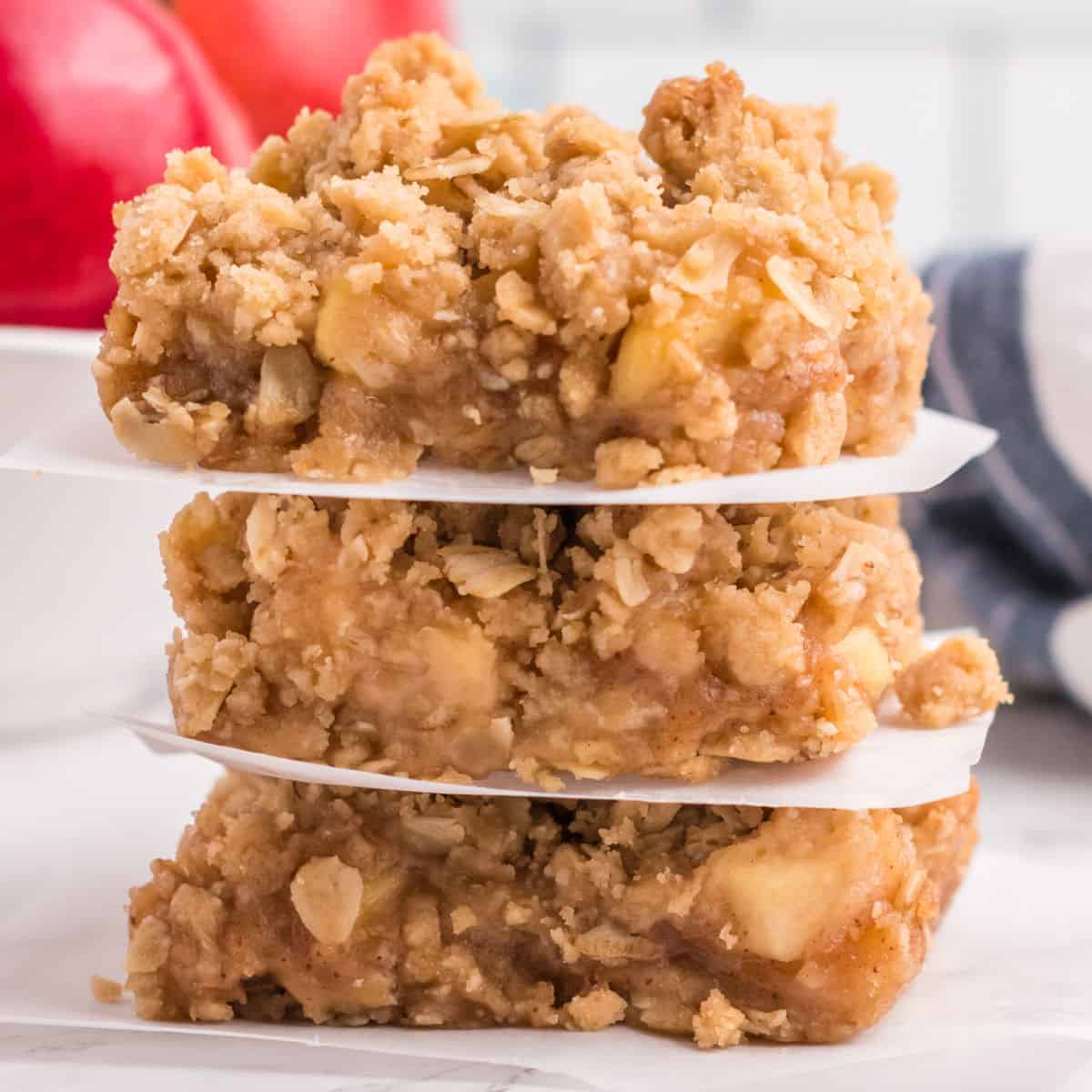 square image of three apple pie oatmeal bars stacked up with parchment paper between each bar