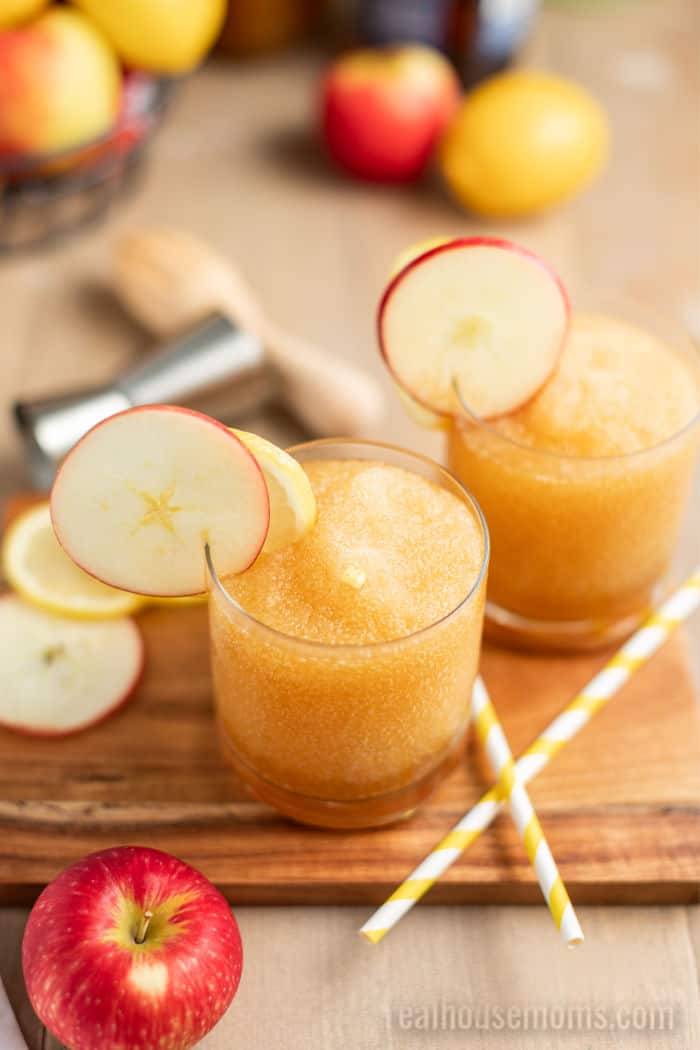 two rocks glasses filled with apple whiskey sour and garnished with a slice of apple and lemon
