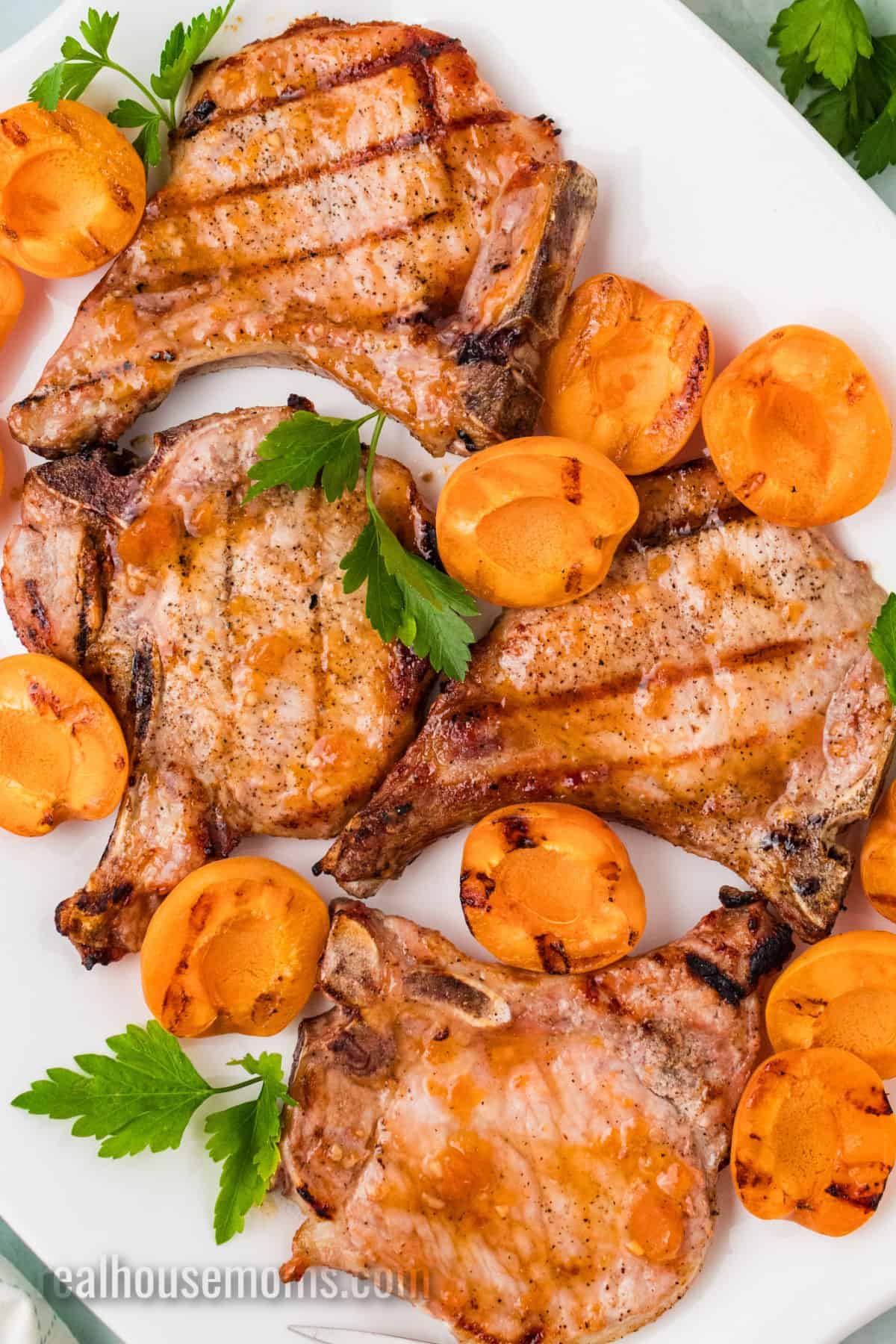 apricot grilled pork chops and grilled apricots on a platter with parsley sprigs
