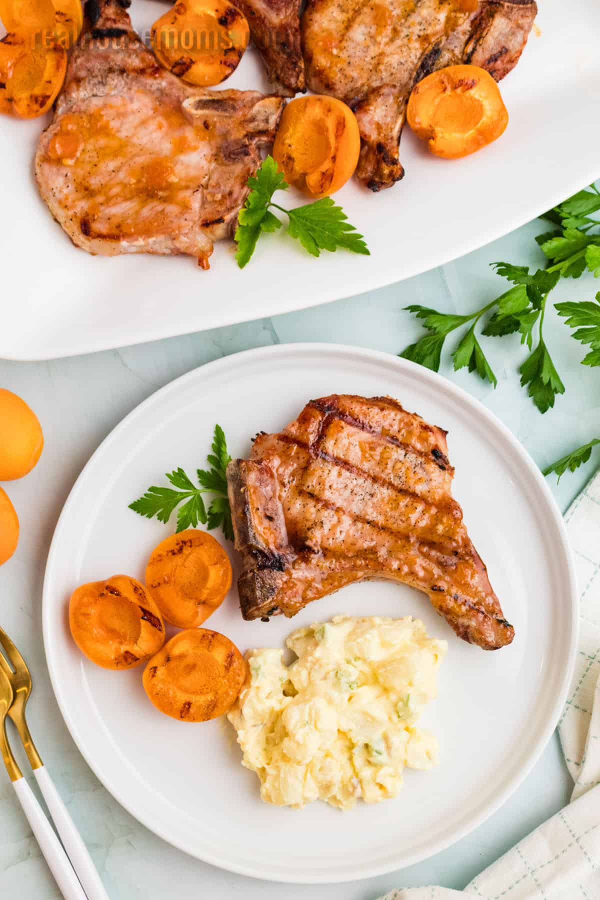 a apricot grilled pork chop on a dinner plate with a few grilled apricot halves and potato salad