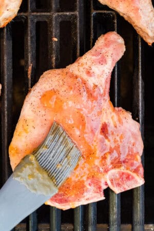 par cooked pork chops being brushed with apricot glaze on the grill