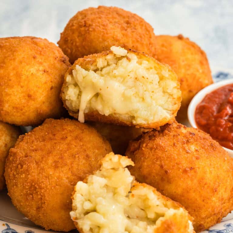 square image of an arancini broken in half to show the gooey cheesy inside