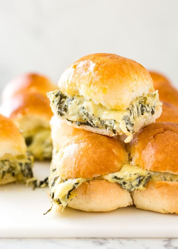 Spinach Artichoke Dip Sliders stacked up on a serving tray with cheese melting out