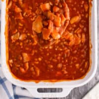 spoon of bbq baked beans over the baking dish with recipe name at the bottom