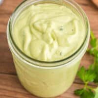 square image of avocado ranch dressing in a mason jar on a cutting board