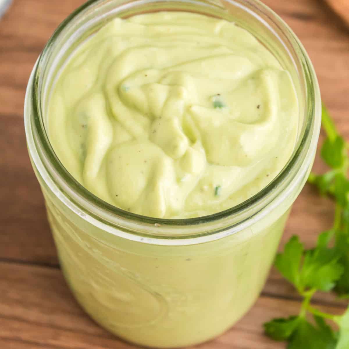 square image of avocado ranch dressing in a mason jar on a cutting board