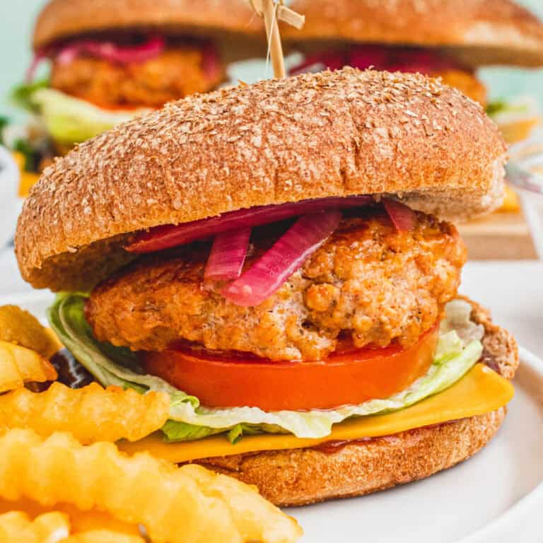 square image of a bbq chicken burger on a plate with french fries