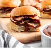 grilled, sliced pork loin on dinner rolls with BBQ sauce on a cutting board
