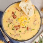 square image of bacon & corn chowder topped with chives in a bowl with a slice of bread