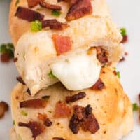 square image of bacon jalapeno cheese bombs on a plate with one cut in half to show cheesy filling