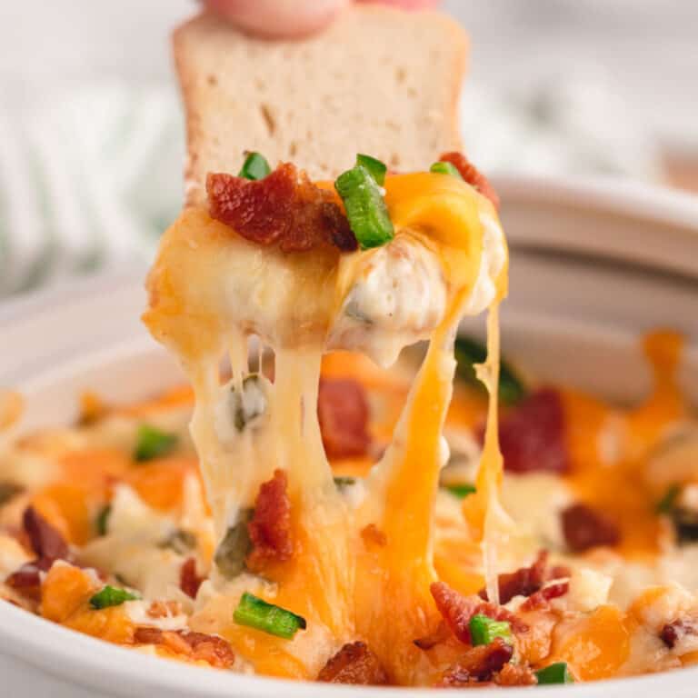 square image of bacon jalapeno popper dip on a cracker with melty cheese above the bowl