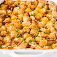 square image of bacon ranch tater tot casserole in a baking dish with bacon, cheese, and green onion on top