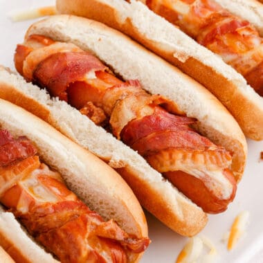 square close up image of bacon wrapped cheese hot dogs on a platter