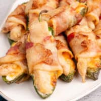 square image of bacon wrapped chicken jalapeno poppers piled on a platter