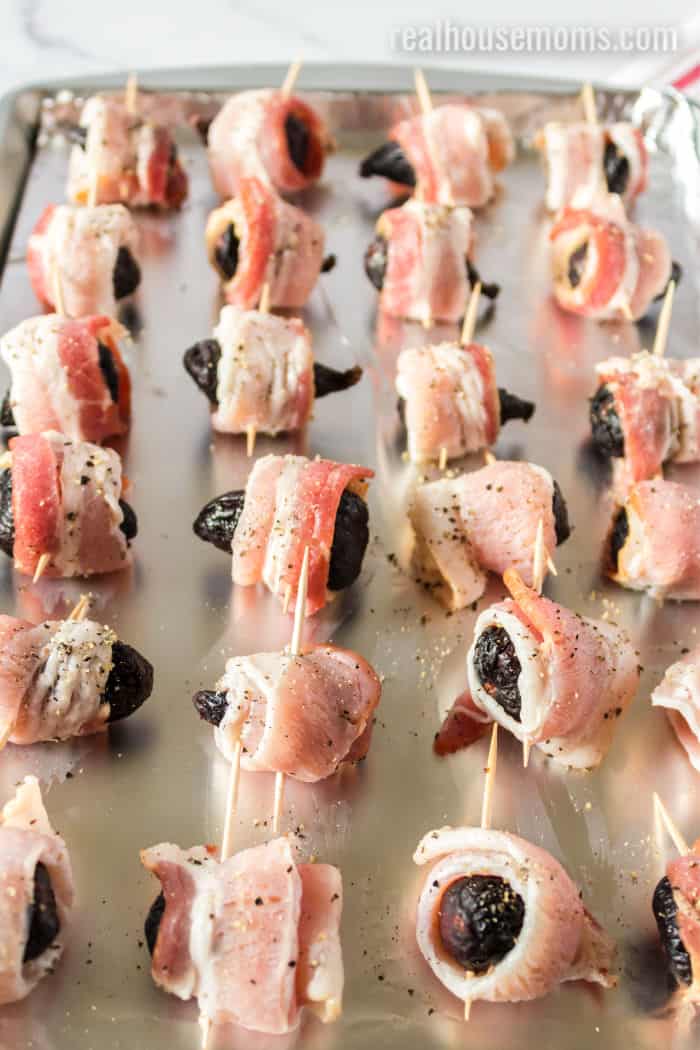 dried figs wrapped in bacon on a foil-lined baking sheet