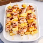 angled view of bacon wrapped shrimp & pineapple kabobs piled on a serving platter