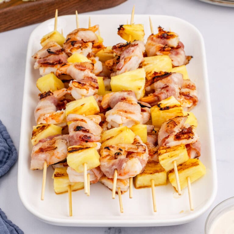 angled view of bacon wrapped shrimp & pineapple kabobs piled on a serving platter