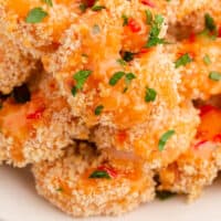 square image of bang bang shrimp piled on a plate with extra sauce spooned over the top with recipe name at bottom
