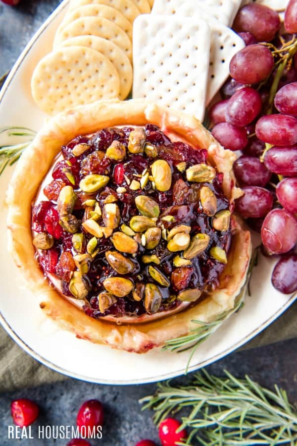 cranberry & pistachio baked brie on a serving platter with crackers and grapes