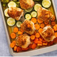 baked chicken thighs with rainbow veggies on a sheet pan with recipe name at the bottom