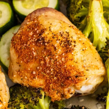 square image of a baked chicken thigh over veggies on a baking sheet