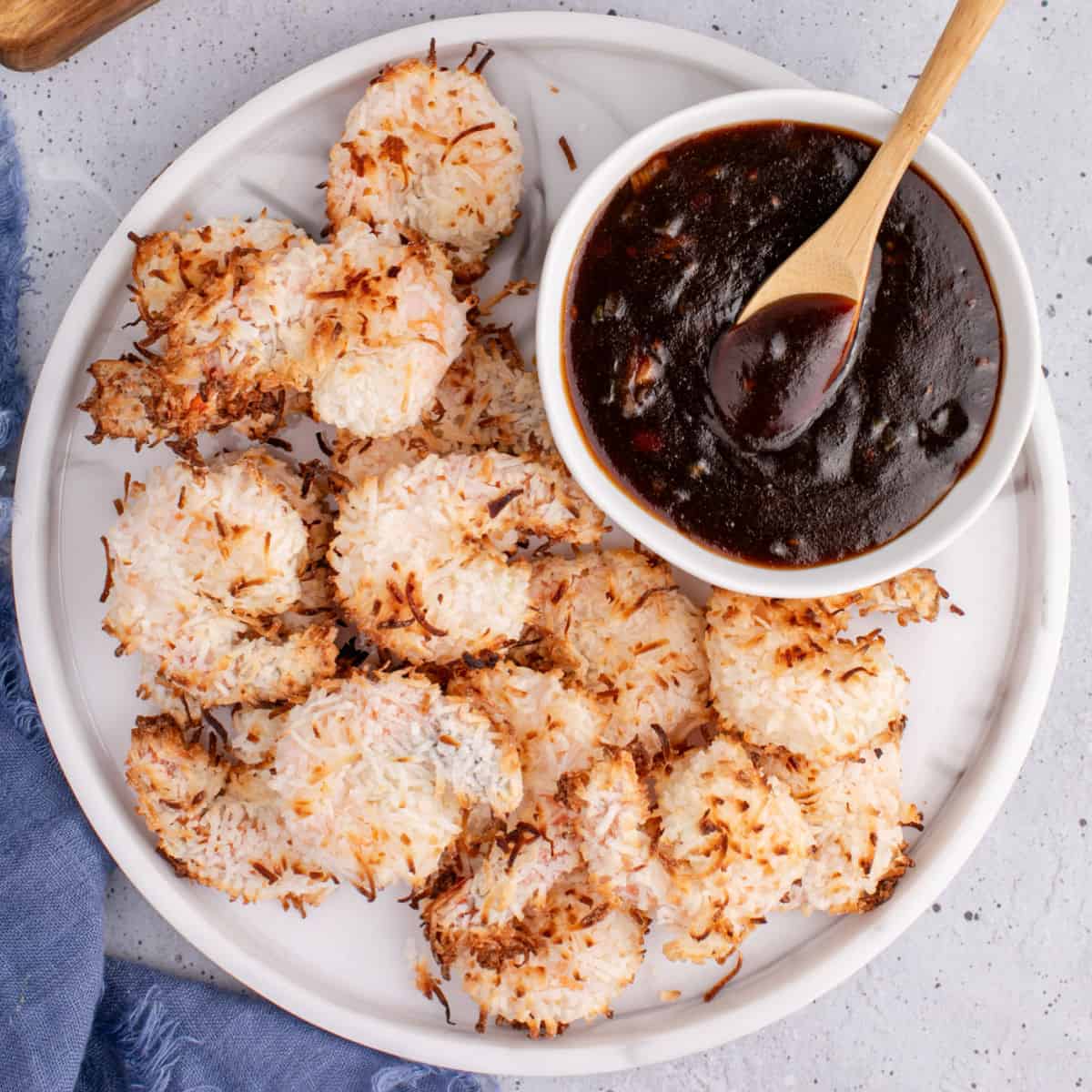 square image of baked coconut shrimp and a bowl of garlic plum sauce on a serving plate
