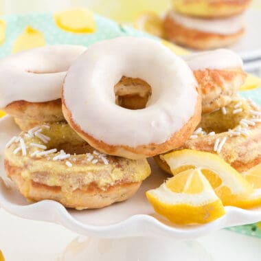 square image of iced baked lemon donuts on a plate with lemon wedges