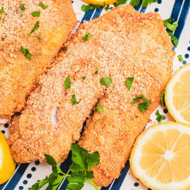 square image of baked parmesan tilapia on a serving platter with lemon slices and parsley
