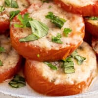 baked parmesan tomatoes piled up on a plate with recipe name at bottom