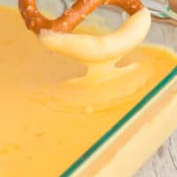 hand dipping a pretzel into baked pepper jack cheese dip with recipe name at the bottom