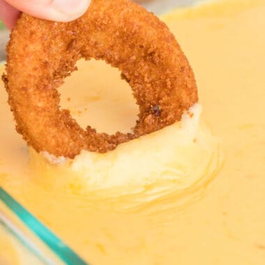 square close up image of an onion ring dipped into baked pepper jack cheese dip