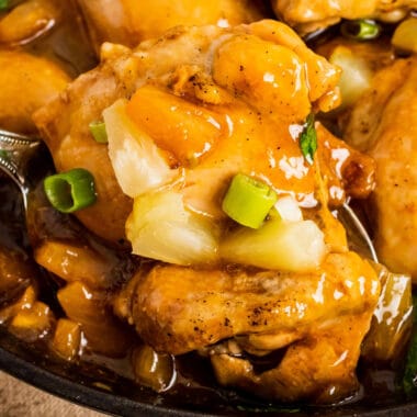 square image of pineapple chicken thighs on a spoon over a skillet