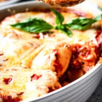 serving spoon with a baked stuffed shell over a baking dish with recipe name at bottom