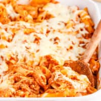 square image of baked ziti in a baking dish with a wooden spoon