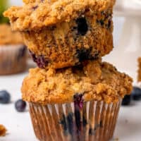two banana blueberry crumb muffins stacked on each other with recipe name at the bottom