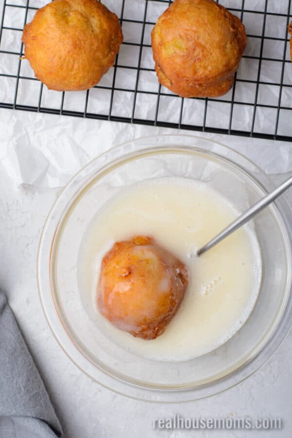 fried banana fritters being dipped in vanilla glaze