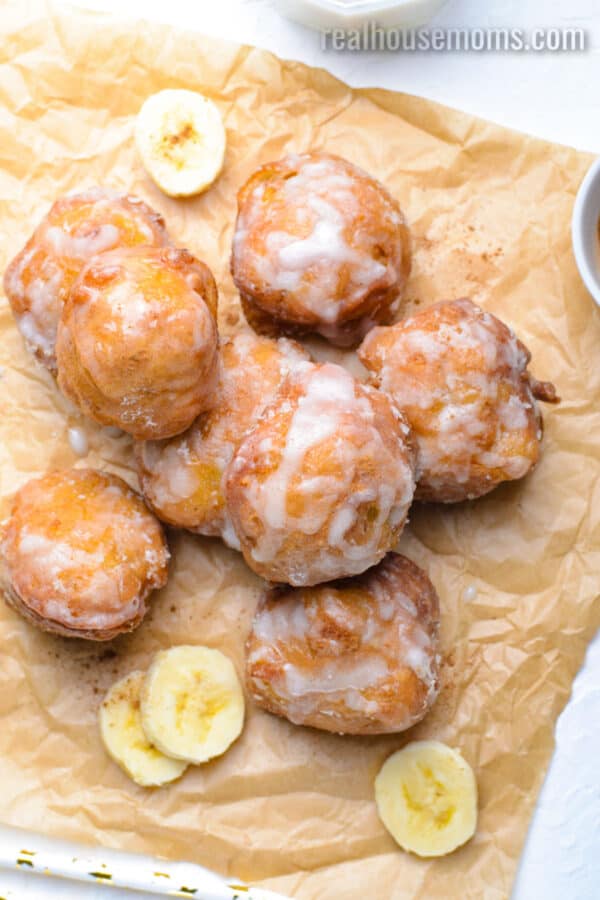 piled of glazed banana fritters on parchment paper with banana slices