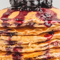 close up image of a stack of banana oatmeal pancakes with berry sauce on a plate with the title of the post on top of the image in blue and black lettering