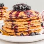 square image of a stack of banana oatmeal pancakes with berry sauce on a plate
