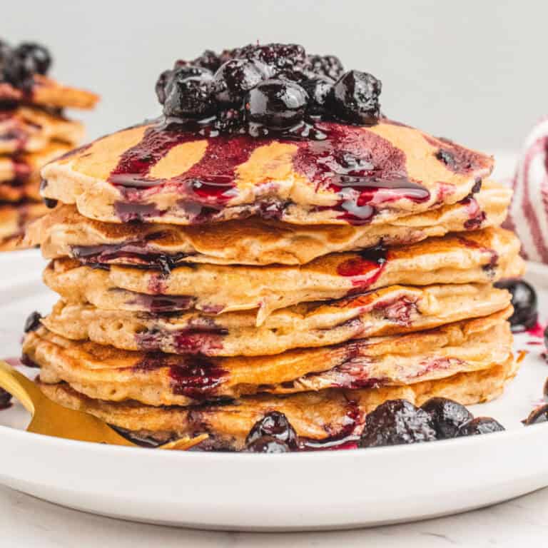 square image of a stack of banana oatmeal pancakes with berry sauce on a plate