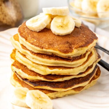square image of banana pancakes stacked up on plate with banana slices on top