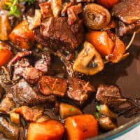 spoonful of beef bourguignon over the pot with recipe name at the bottom