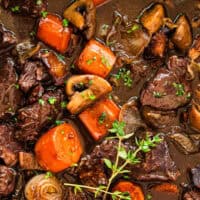 image of beef bourguignon in a large pot with a sprig of thyme for garnish with the title of the post on top with blue and black lettering